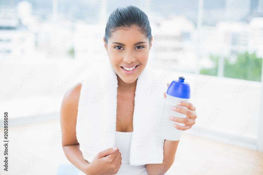 Smiling toned brunette with towel holding sports bottle Smiling toned brunette with towel holding sports bottle