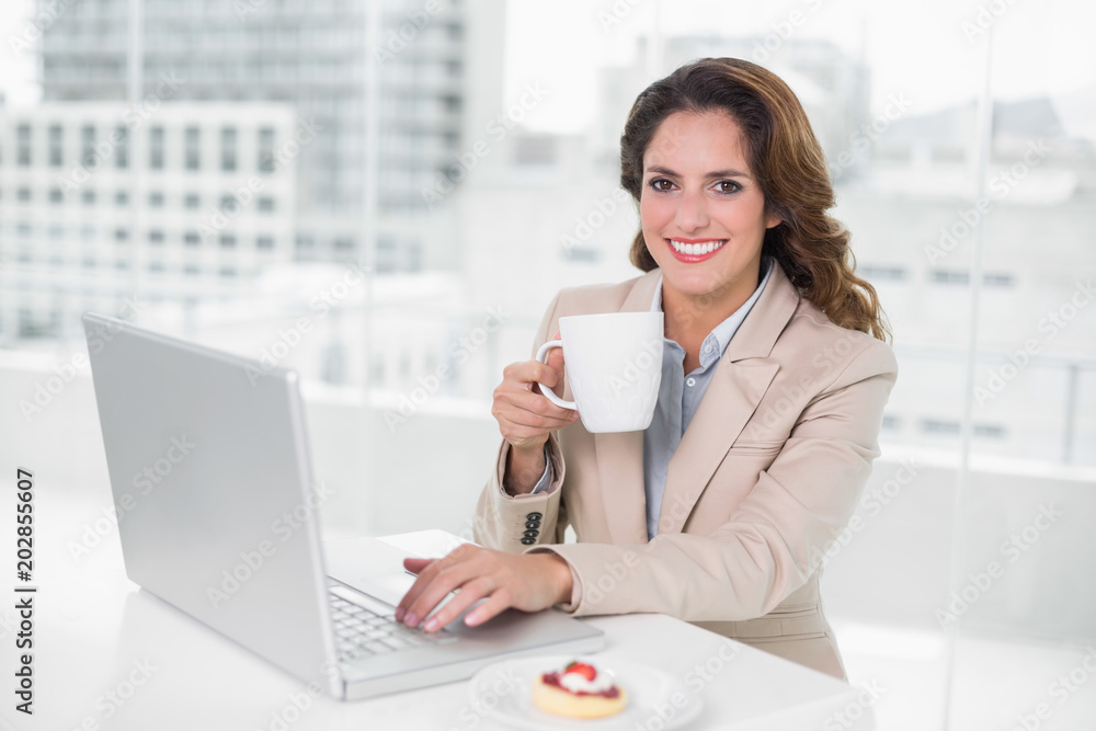 Smiling businesswoman using laptop at her desk and holding mug Smiling businesswoman using laptop at her desk and holding mug