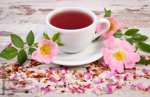 Cup of tea with wild rose flower on rustic wooden background
