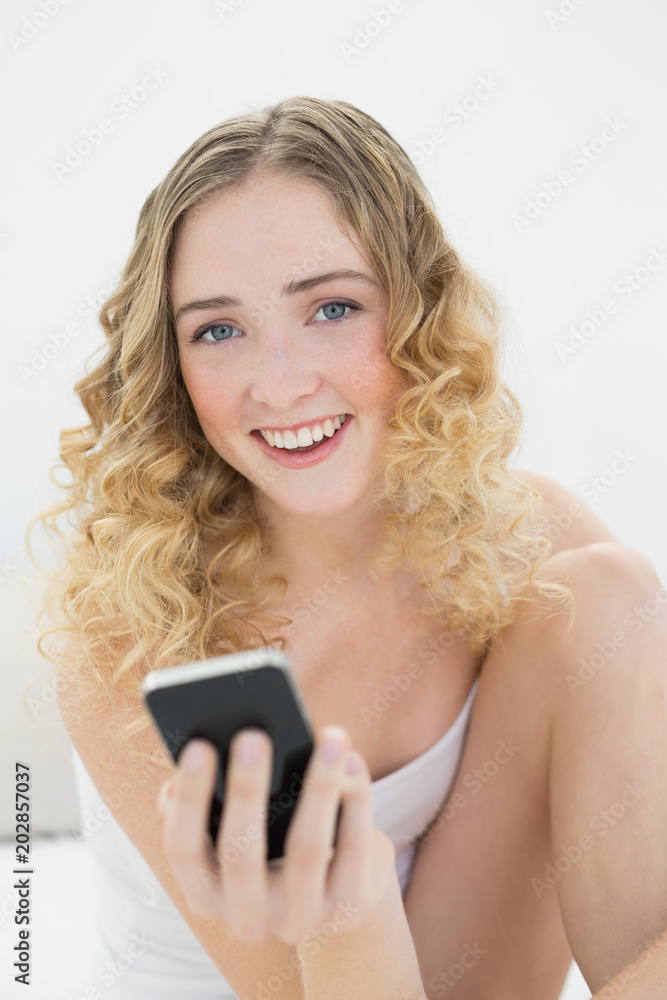 Pretty blonde sitting on bed holding smartphone Pretty blonde sitting on bed holding smartphone