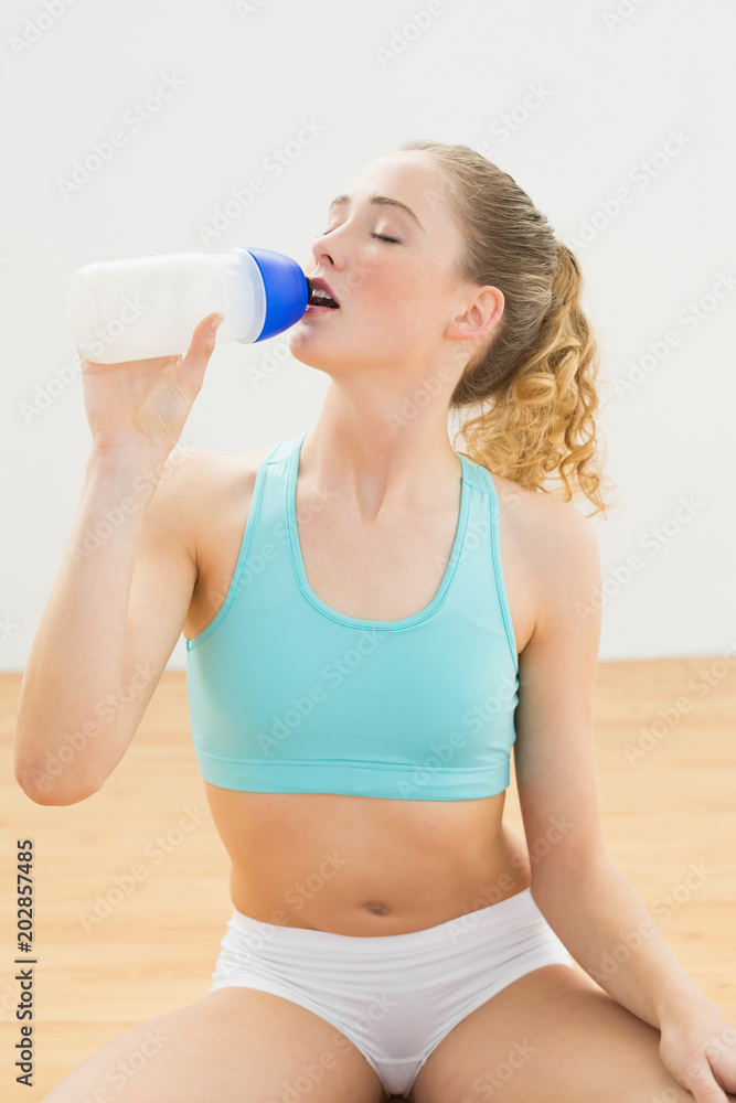 Peaceful slim blonde sitting on floor drinking from sports bottle Peaceful slim blonde sitting on floor drinking from sports bottle