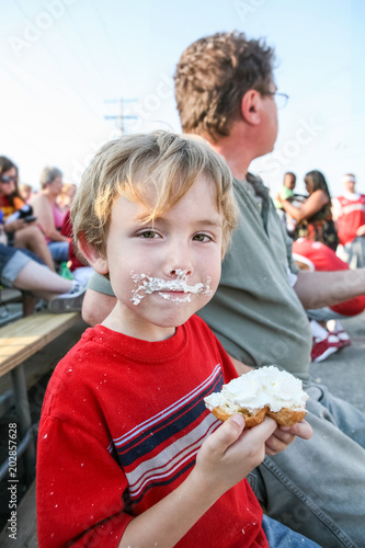 Fotografija Young boy eating a whipped cream puff pastry at the fair