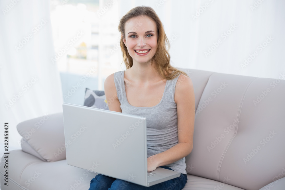 Smiling young woman sitting on couch using laptop Smiling young woman sitting on couch using laptop