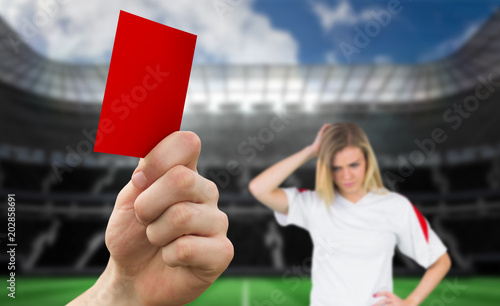 Hand holding up red card against large football stadium with empty stands with fan