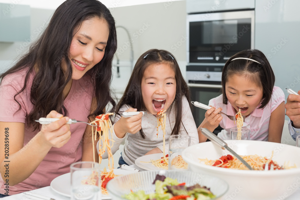 Woman with kids enjoying spaghetti lunch in kitchen Woman with kids enjoying spaghetti lunch in kitchen