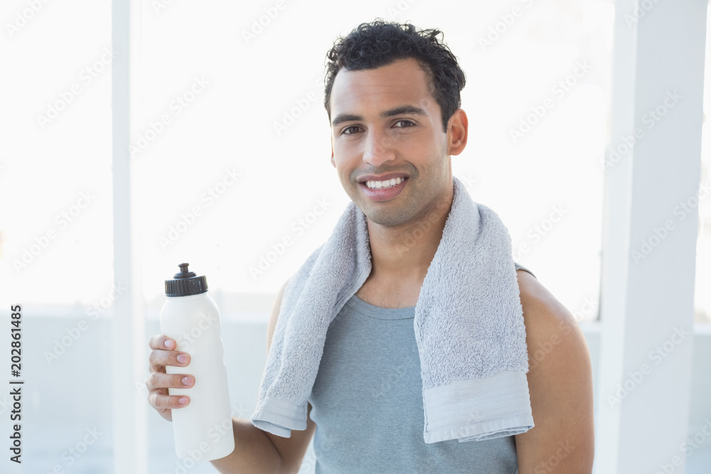 Man with towel around neck holding water bottle in fitness studio