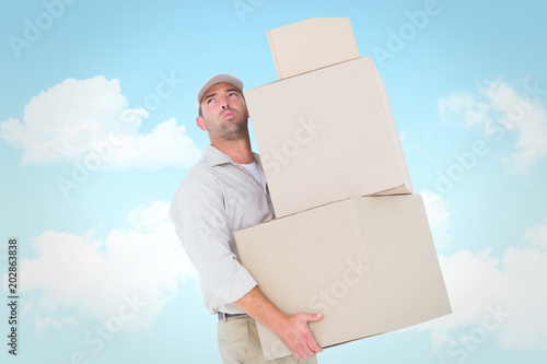 Tired delivery man carrying stack boxes against blue sky