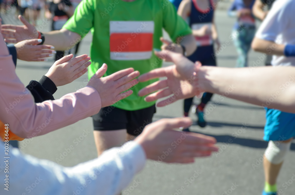 Marathon running race, support runners on road, child's hand giving highfive, sport concept
Marathon running race, support runners on road, child's hand giving highfive, sport concept