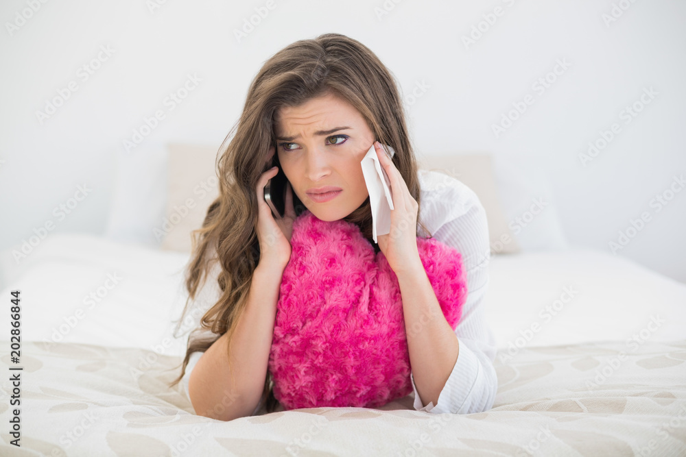 Disappointed casual brown haired woman in white pajamas making a phone call Disappointed casual brown haired woman in white pajamas making a phone call