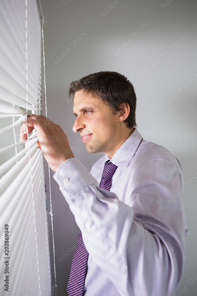 Young businessman peeking through blinds in office