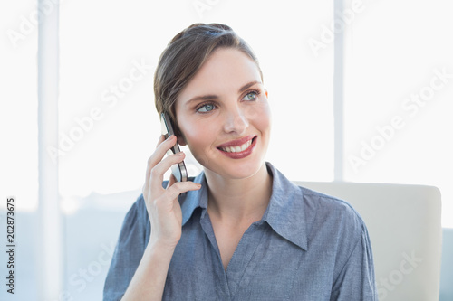 Content lovely businesswoman phoning with her smartphone sitting at her desk