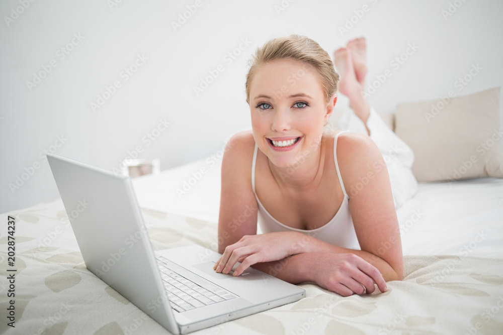 Natural happy blonde using laptop and lying on bed Natural happy blonde using laptop and lying on bed