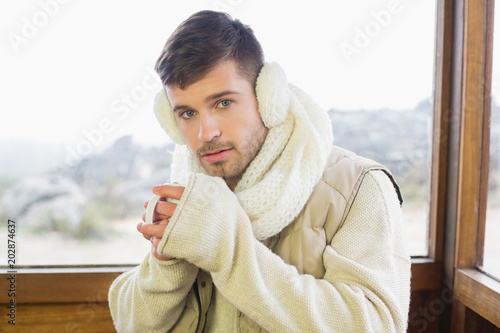 Man wearing earmuff while drinking coffee against window