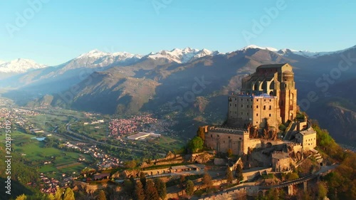 Aerial: drone flying at old medieval abbey perched on mountain top, background snowy Alps at sunrise. Sacra di San Michele (italian) - Saint Michel Abbey (english traslation) - Turin, Italy  photo