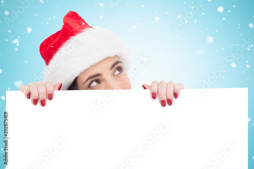 Pretty brunette in santa hat showing white poster against blue vignette