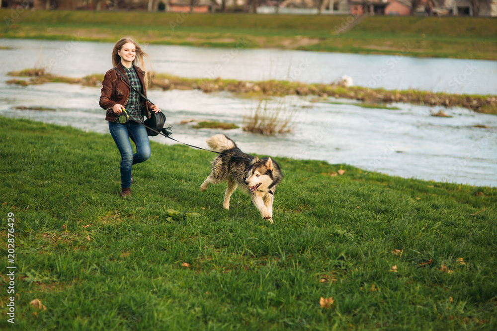 A girl is walking with a dog along the embankment. Beautiful Husky dog. The river. Spring