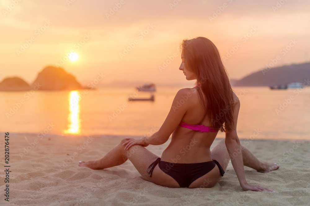 Situatie Grit wereld Rear view of slim female model sitting on seashore wearing bikini looking  away during sunrise with sun path reflected water Stock Photo | Adobe Stock