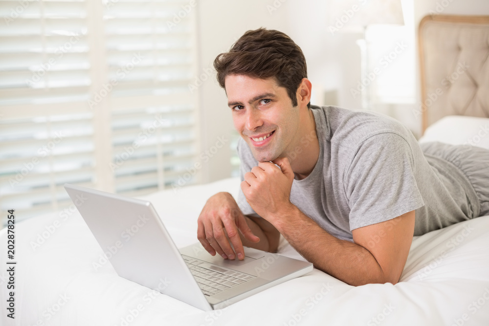Casual smiling young man using laptop in bed Casual smiling young man using laptop in bed