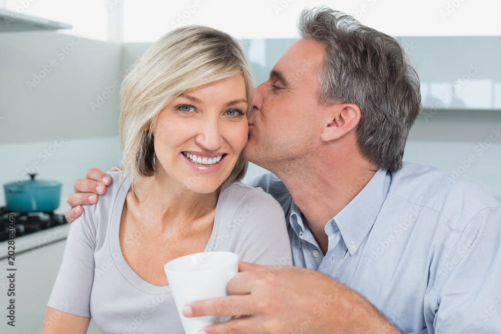 Man kissing a happy womans cheek in kitchen Man kissing a happy womans cheek in kitchen