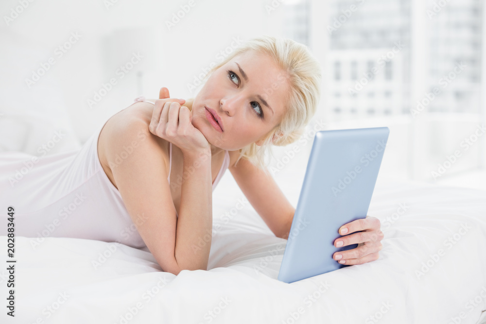 Thoughtful casual blond with tablet PC lying in bed Thoughtful casual blond with tablet PC lying in bed