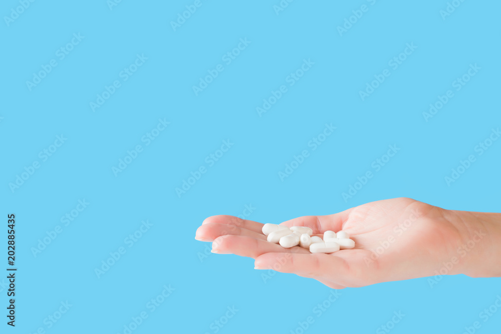 White pills in woman's hand. Receiving vitamins or medicaments. Medical, pharmacy and healthcare concept. Copy space. Empty place for text or logo on blue background.