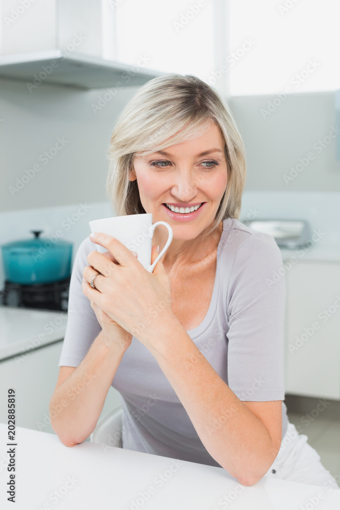 Thoughtful smiling woman with coffee cup in kitchen Thoughtful smiling woman with coffee cup in kitchen