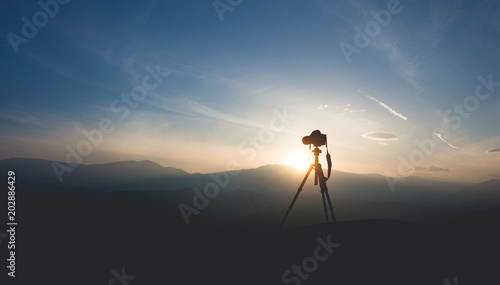 Silhouette of a camera on a tripod. Shooting sunset in the mountains