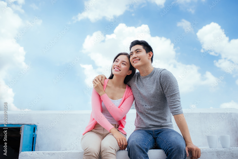 Young beautiful woman and asian man laugh against the dark blue sky with clouds