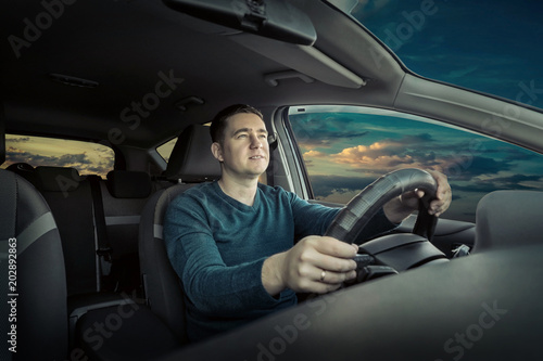 Man sitting and driving in the car under sunset sky © Andrii IURLOV