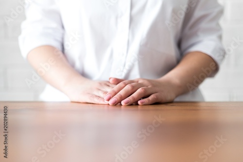 Girl folded her hands on a wooden table closeup