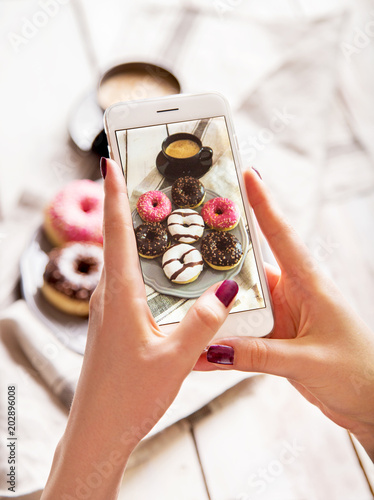 Woman photographing breakfast with coffee and donuts. Taking food photo with mobile phone.