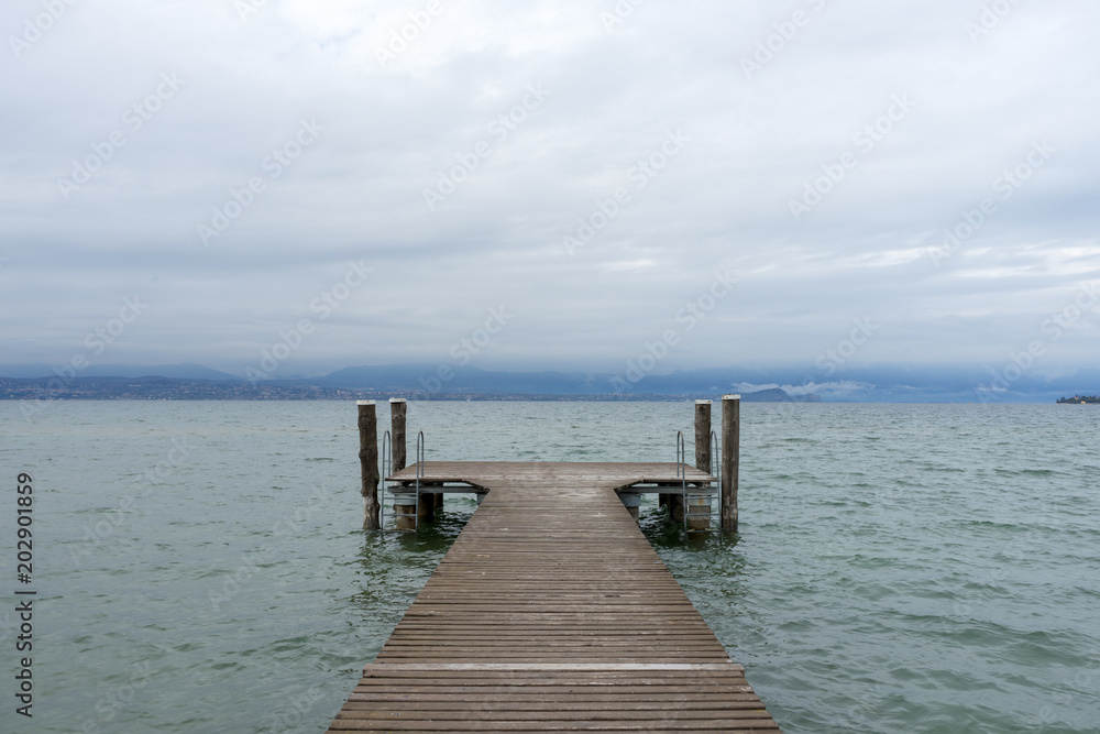 Pier on the Lake di Garda, italy, with snow capped mountains and clouds in the background