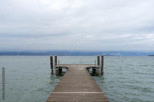 Pier on the Lake di Garda, italy, with snow capped mountains and clouds in the background