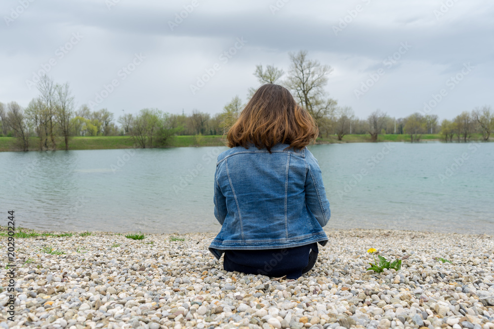 Fototapeta premium Young girl sitting on rocks looking at lake
