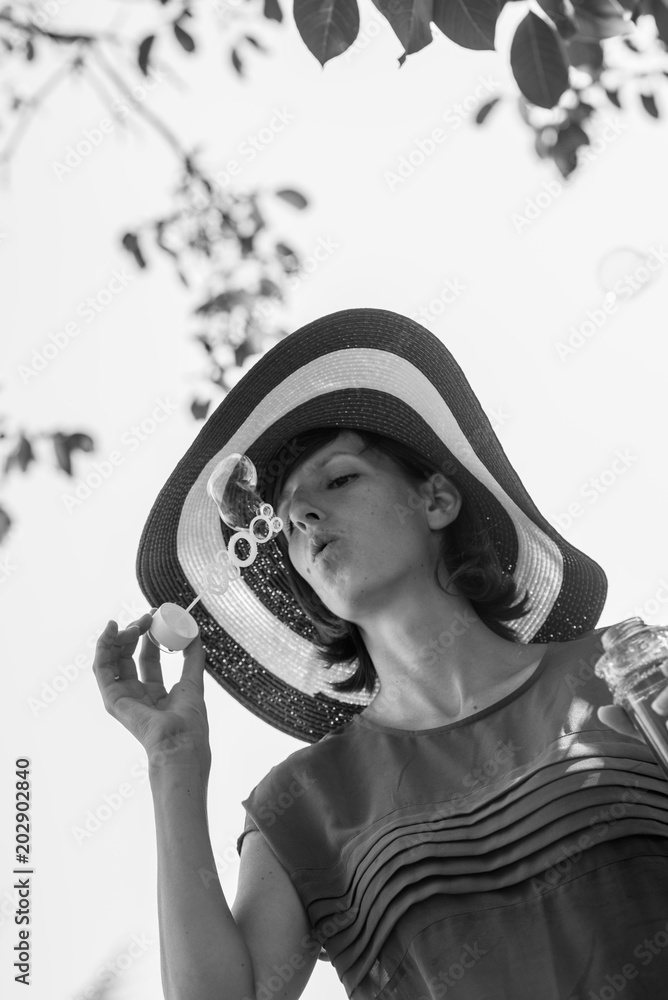Φωτογραφία Greyscale portrait of an attractive woman in a wide brimmed sunhat blowing bubbl