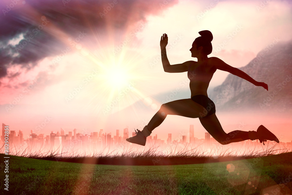 Fit brunette running and jumping against sun shining over city