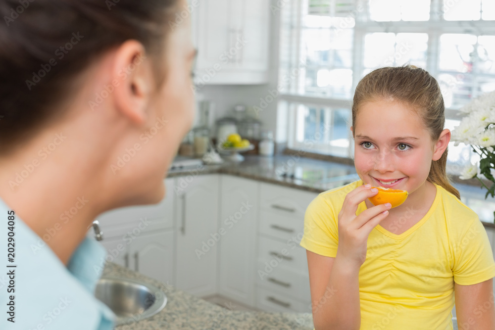Girl having orange while looking at mother Girl having orange while looking at mother