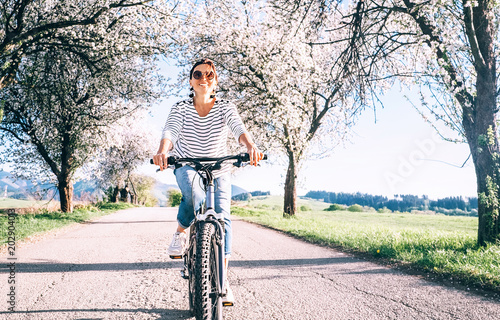 Happy smiling woman rides a bicycle on the country road under blossom trees