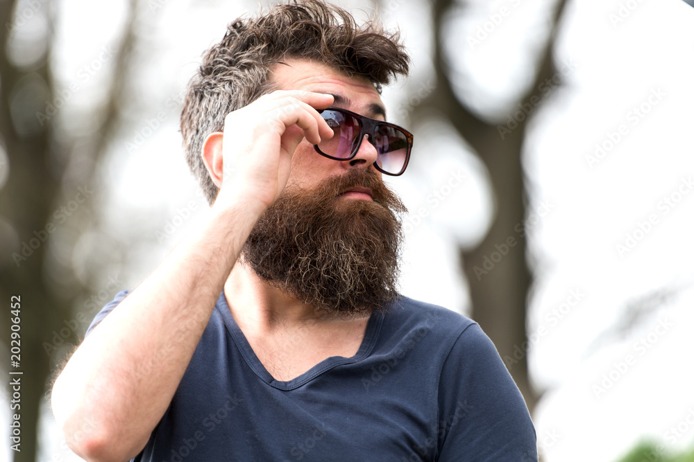 Side view bearded man adjusting his sunglasses. Stylish young man with well-trimmed beard and mustache enjoying warm spring day in park Side view bearded man adjusting his sunglasses. Stylish young man with well-trimmed beard and mustache enjoying warm spring day in park