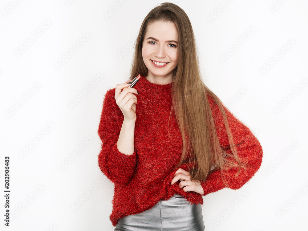 Spectacular blonde woman in red blouse silver leather pants posing with lipstick in front of white wall. Graceful girl gorgeous long hair having fun on photoshoot.