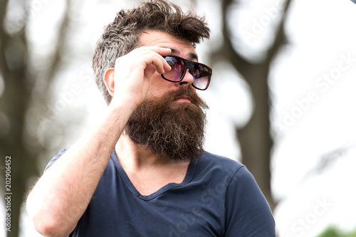 Side view bearded man adjusting his sunglasses. Stylish young man with well-trimmed beard and mustache enjoying warm spring day in park