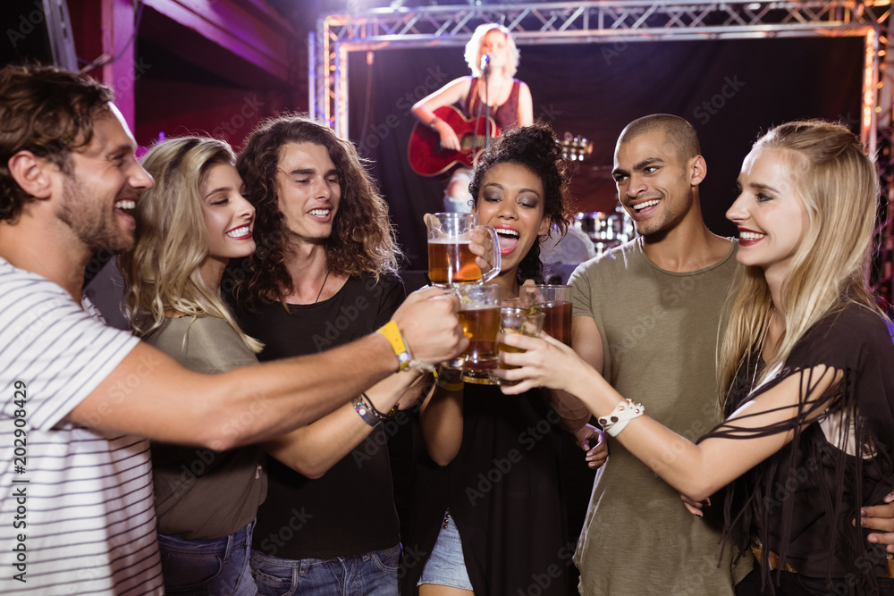 Smiling friends toasting beer glasses with performer singing in background