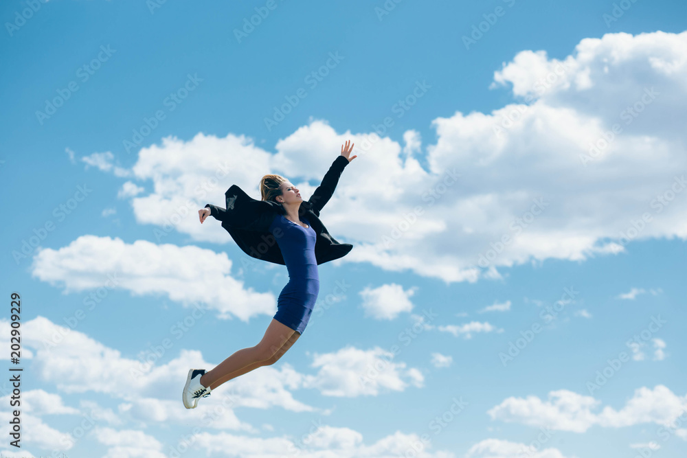 a woman jumping high, wearing a blue dress against the blue sky with clouds. A woman is flying against the sky