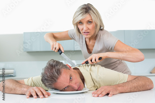Angry woman holding knife to mans neck in kitchen