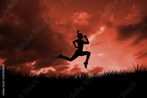 Fit brunette running and jumping against red sky over grass