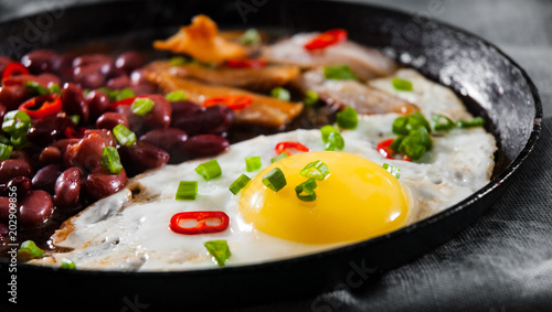 fried egg with bacon and red beans in a frying pan on wooden table