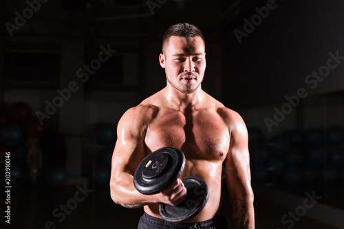 Handsome power athletic man with dumbbell. Strong bodybuilder with six pack, perfect abs, shoulders, biceps, triceps and chest