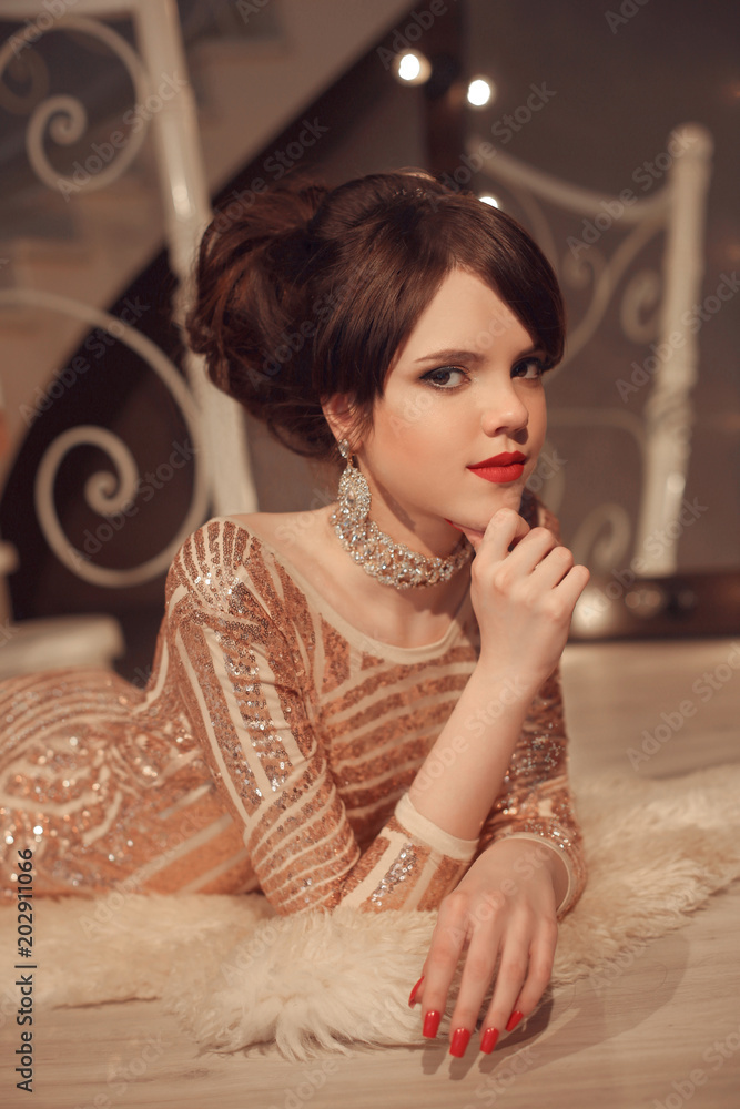 Fashionable young girl posing in golden dress at graduation prom party. Teen  brunette with elegant hairstyle posing by modern staircase in luxury  interior. Stock Photo | Adobe Stock