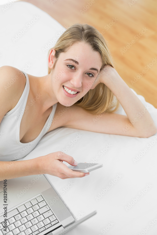 Obraz premium Gleeful blonde woman lying on her bed using her smartphone
