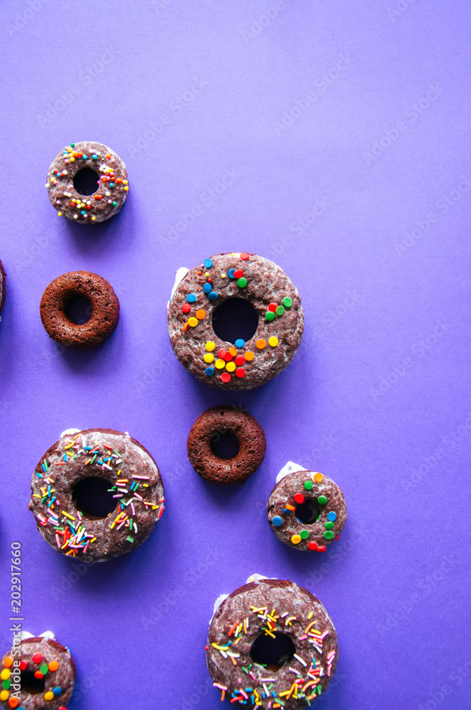 Chocolate baked doughnuts on a violet background glazed and decorated with confetti. Top view. Chocolate baked doughnuts on a violet background glazed and decorated with confetti. Top view.